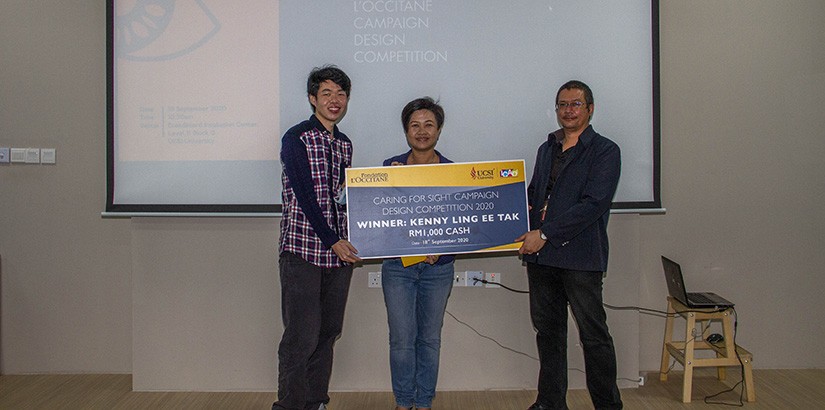 Dr Khairul (for right) handing out a cash prize mock cheque to a student for winning at the L’occitane Campaign Design Competition held in 2020. 