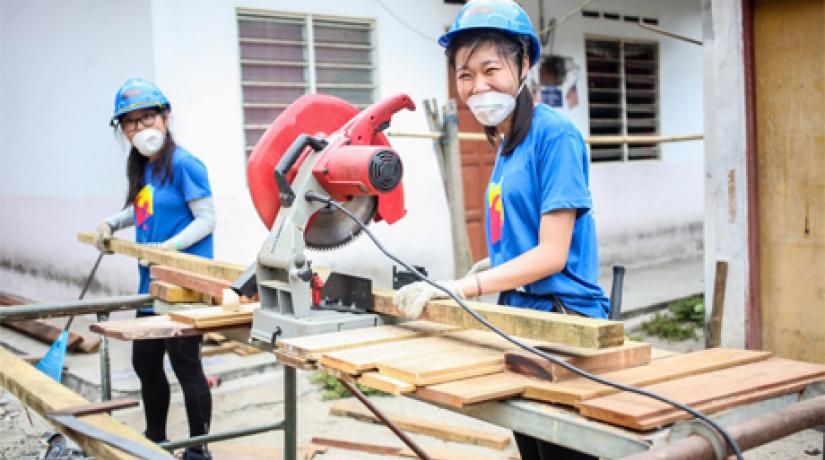  Students working on planks of wood to build a house for an aboriginal (Orang Asli) family.