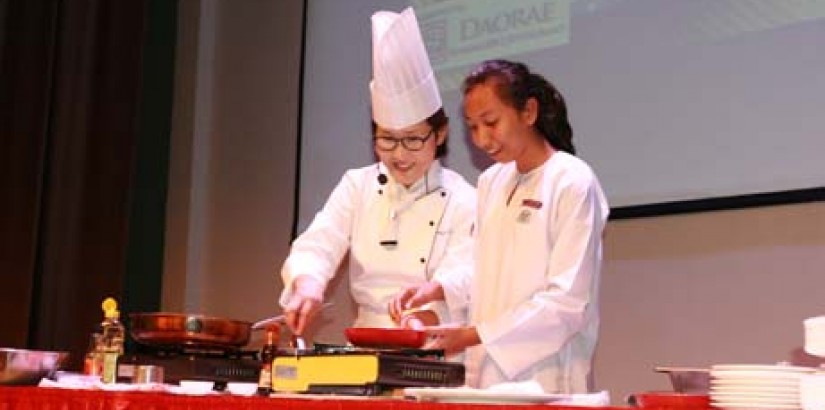 Woosong University (Korea) master chef and specialist of Korean royal cuisine Professor Dr Shin Mi Kyung conducting a Korean culinary presentation with a visiting secondary school student after the MoU exchange ceremony.
